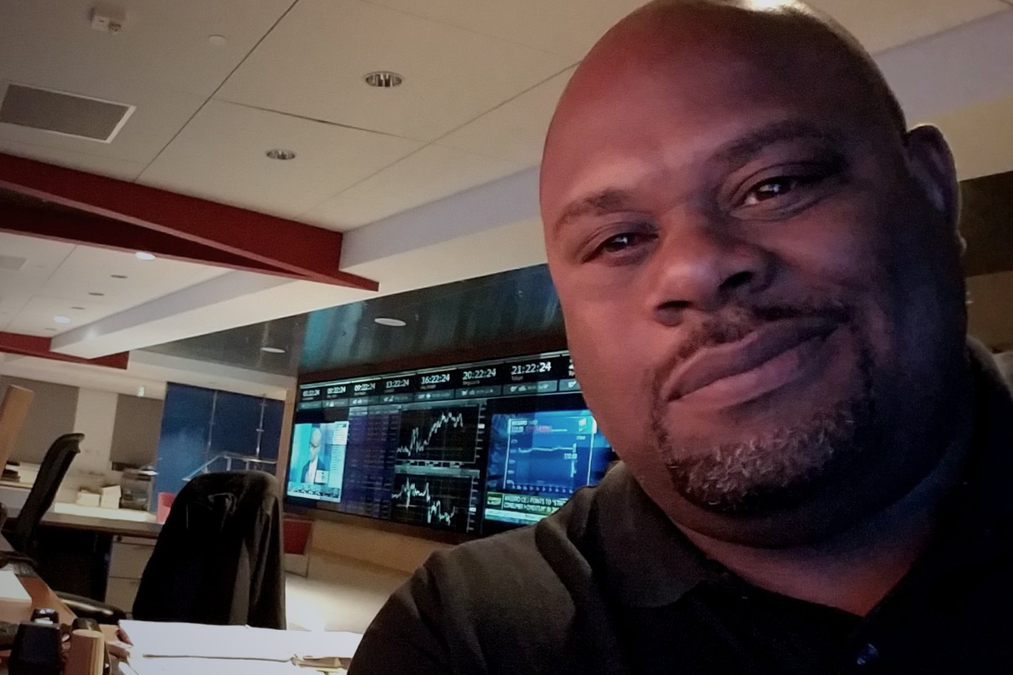 Travis Lewis on the trading floor, market displays behind him